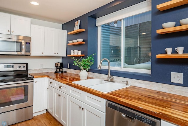 kitchen featuring wooden counters, sink, stainless steel appliances, and white cabinetry