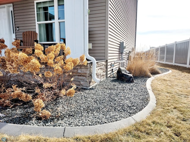 view of side of home featuring stone siding and fence