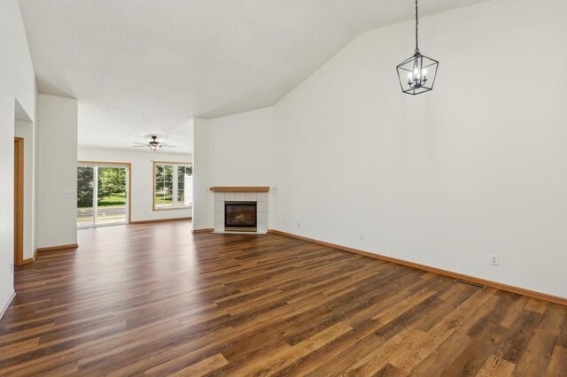 unfurnished living room featuring a tiled fireplace, lofted ceiling, ceiling fan with notable chandelier, and dark hardwood / wood-style floors