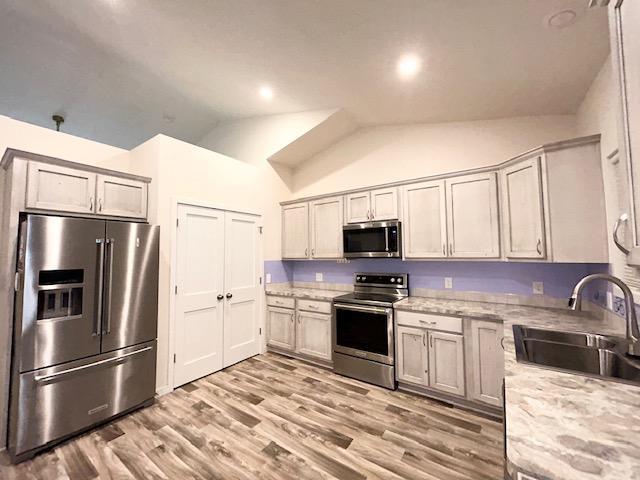 kitchen with lofted ceiling, sink, light wood-type flooring, light stone countertops, and stainless steel appliances