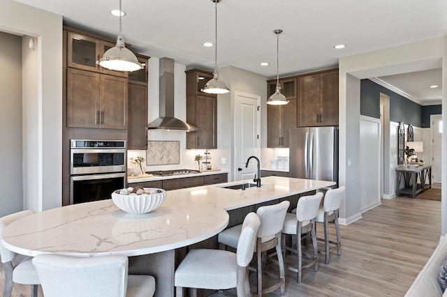 kitchen featuring pendant lighting, sink, appliances with stainless steel finishes, an island with sink, and wall chimney exhaust hood