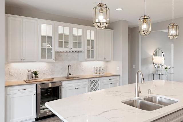 kitchen with beverage cooler, white cabinets, hanging light fixtures, and sink