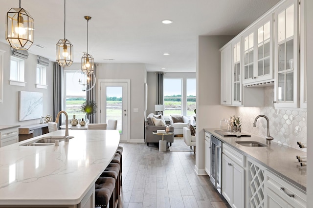 kitchen with sink, hanging light fixtures, white cabinets, and an island with sink