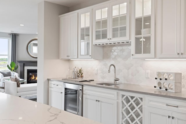 kitchen with decorative backsplash, beverage cooler, light stone countertops, white cabinets, and sink