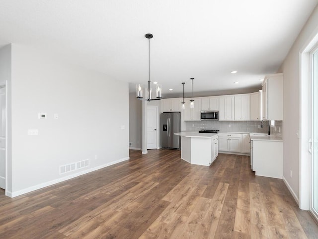 kitchen with decorative light fixtures, a kitchen island, decorative backsplash, white cabinetry, and appliances with stainless steel finishes