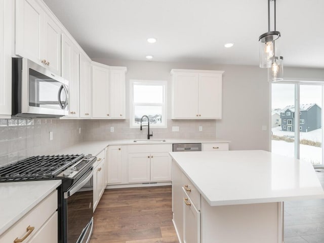 kitchen with decorative light fixtures, a center island, sink, white cabinetry, and appliances with stainless steel finishes