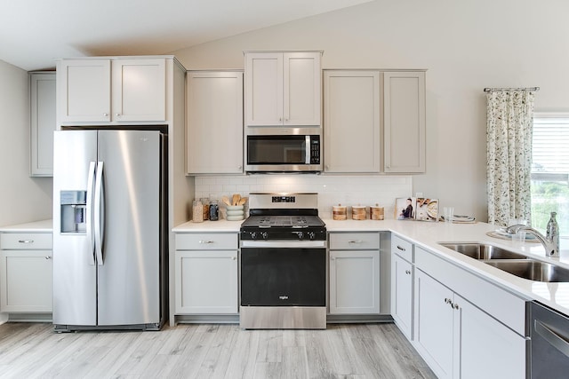 kitchen with lofted ceiling, sink, appliances with stainless steel finishes, light hardwood / wood-style floors, and backsplash