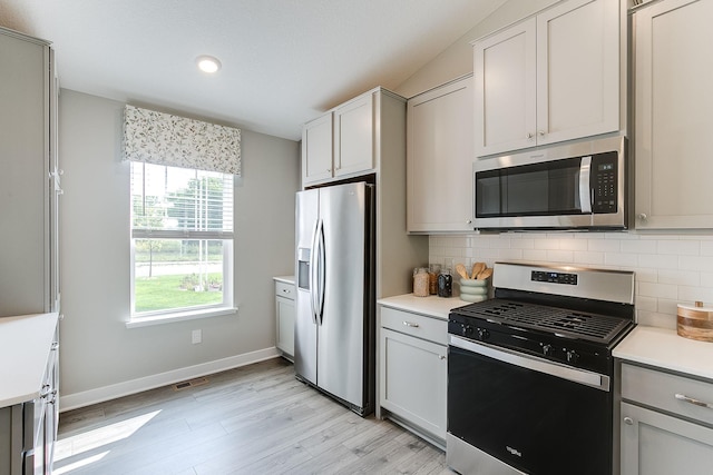 kitchen with vaulted ceiling, gray cabinets, stainless steel appliances, light hardwood / wood-style floors, and decorative backsplash