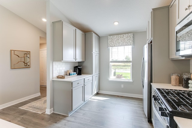 kitchen featuring gray cabinets, vaulted ceiling, appliances with stainless steel finishes, and light wood-type flooring