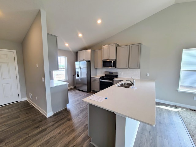 kitchen featuring sink, appliances with stainless steel finishes, gray cabinetry, vaulted ceiling, and kitchen peninsula