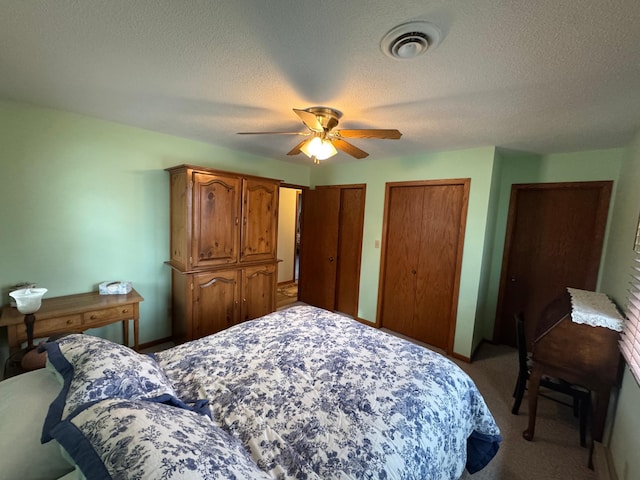 bedroom featuring ceiling fan, a textured ceiling, carpet flooring, and multiple closets