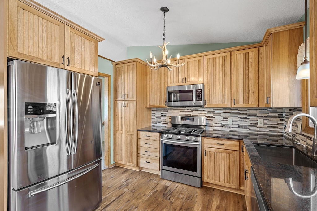 kitchen with appliances with stainless steel finishes, a notable chandelier, decorative light fixtures, vaulted ceiling, and sink