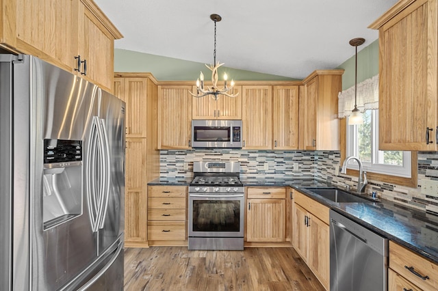 kitchen featuring lofted ceiling, pendant lighting, sink, appliances with stainless steel finishes, and a chandelier