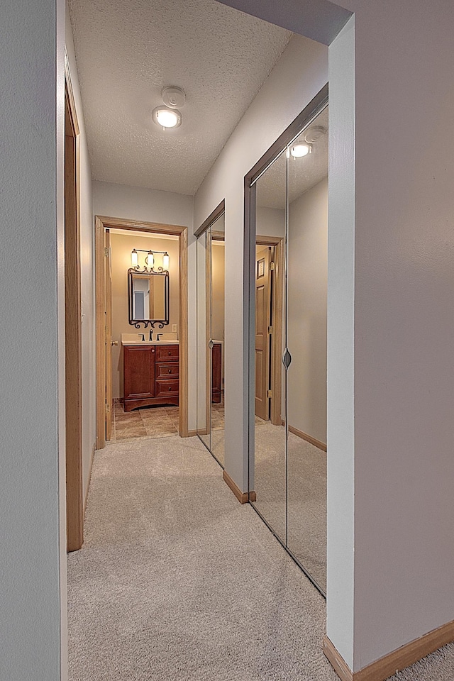 hall featuring sink, light colored carpet, and a textured ceiling