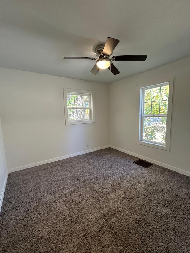 empty room featuring a ceiling fan, visible vents, dark carpet, and baseboards