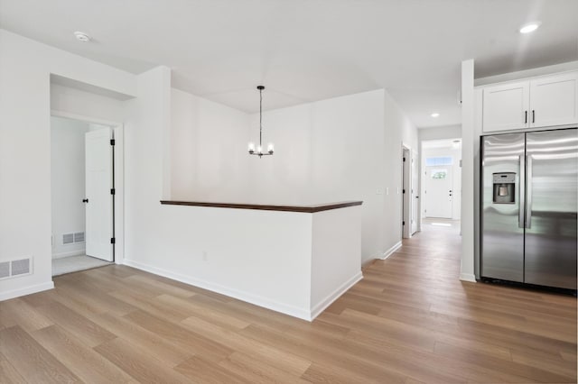 kitchen with stainless steel fridge, decorative light fixtures, white cabinets, light hardwood / wood-style floors, and an inviting chandelier