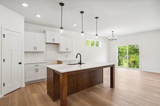 kitchen with tasteful backsplash, white cabinetry, a kitchen island with sink, sink, and decorative light fixtures