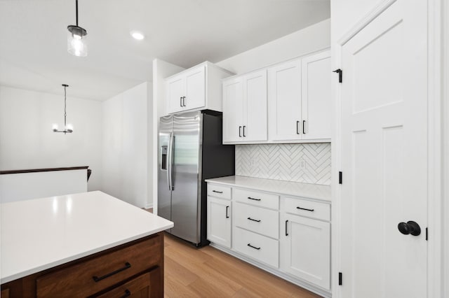 kitchen with pendant lighting, white cabinets, stainless steel refrigerator with ice dispenser, light hardwood / wood-style floors, and backsplash