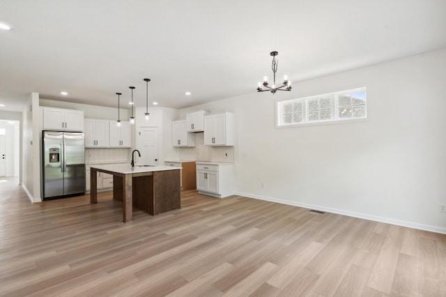 kitchen featuring stainless steel refrigerator with ice dispenser, hanging light fixtures, white cabinets, and a center island with sink