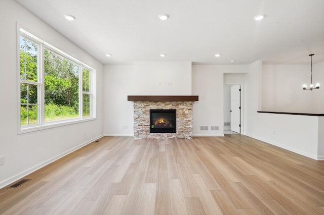 unfurnished living room with light hardwood / wood-style flooring, a stone fireplace, and a notable chandelier