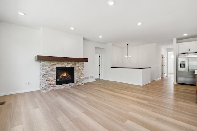 unfurnished living room featuring light wood-type flooring, a chandelier, and a fireplace