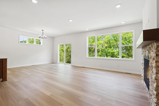 unfurnished living room featuring an inviting chandelier, light hardwood / wood-style floors, and a fireplace