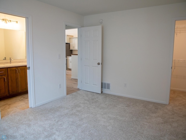 unfurnished bedroom with ensuite bath, a walk in closet, light carpet, sink, and a closet