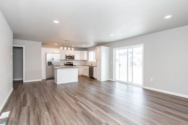 kitchen with a center island, hardwood / wood-style floors, appliances with stainless steel finishes, white cabinetry, and hanging light fixtures