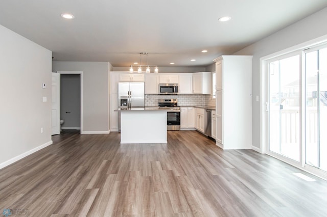 kitchen featuring white cabinets, appliances with stainless steel finishes, a kitchen island, decorative backsplash, and hanging light fixtures