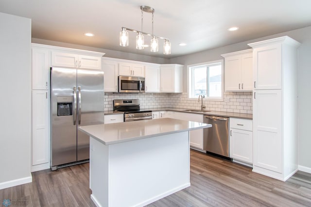 kitchen with hanging light fixtures, appliances with stainless steel finishes, white cabinets, a kitchen island, and light hardwood / wood-style floors