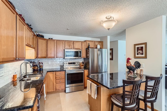 kitchen with dark stone countertops, decorative backsplash, sink, appliances with stainless steel finishes, and a breakfast bar area