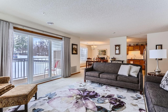 living room featuring light colored carpet, a textured ceiling, sink, and an inviting chandelier