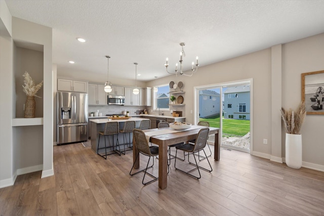 dining area featuring sink, an inviting chandelier, a textured ceiling, and light hardwood / wood-style floors