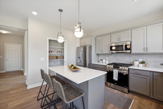 kitchen with appliances with stainless steel finishes, decorative light fixtures, wood-type flooring, decorative backsplash, and gray cabinets