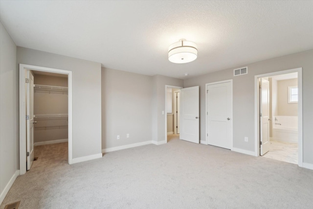 unfurnished bedroom with ensuite bathroom, light carpet, a spacious closet, and a closet