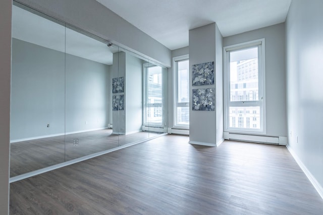 empty room featuring a baseboard heating unit, dark hardwood / wood-style flooring, and a wealth of natural light