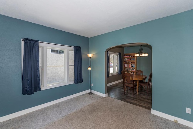 spare room featuring carpet floors, baseboards, arched walkways, and a chandelier