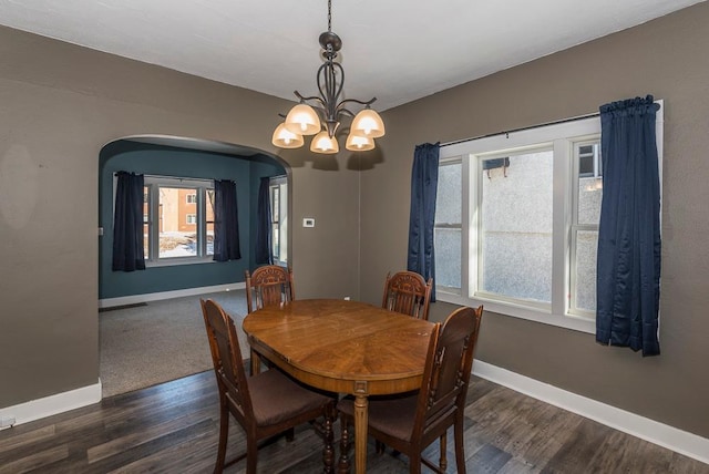 dining room featuring arched walkways, dark wood-style flooring, an inviting chandelier, and baseboards