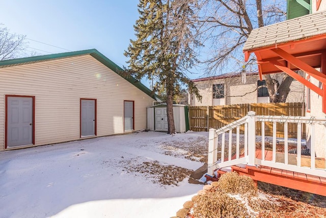 yard covered in snow featuring an outbuilding, a storage unit, and fence