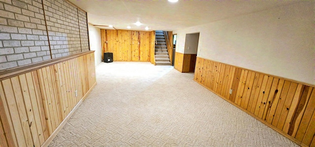 hall featuring light carpet, wood walls, stairs, and a wainscoted wall