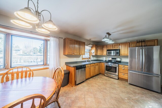 kitchen with stainless steel appliances, dark countertops, hanging light fixtures, an inviting chandelier, and brown cabinetry