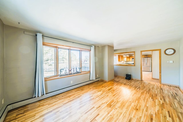 spare room featuring a baseboard radiator, wood finished floors, and baseboards