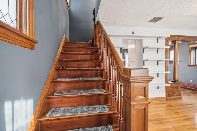 stairs with wood-type flooring, a textured ceiling, and ornate columns