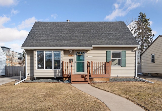 view of front facade with roof with shingles, a front yard, and fence