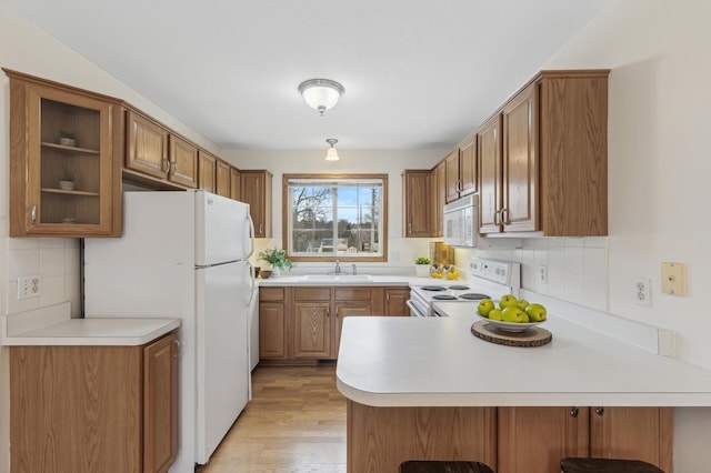 kitchen with sink, kitchen peninsula, white appliances, light hardwood / wood-style floors, and decorative backsplash