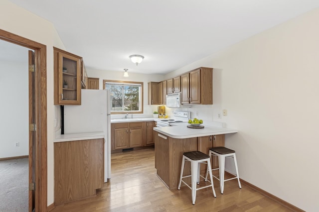 kitchen with sink, white appliances, light hardwood / wood-style flooring, a kitchen breakfast bar, and kitchen peninsula