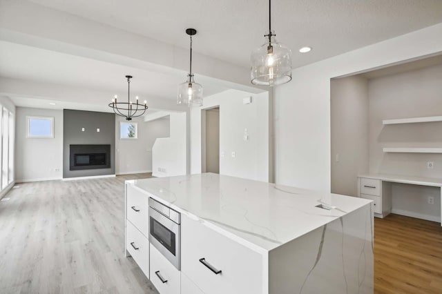 kitchen with stainless steel microwave, decorative light fixtures, light stone countertops, a large island, and white cabinets