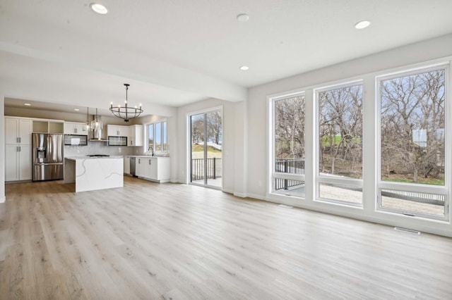 unfurnished living room with sink, light hardwood / wood-style floors, and a notable chandelier