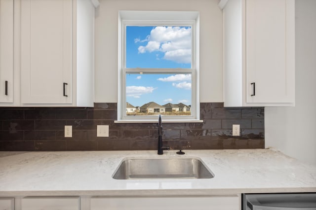 kitchen featuring dishwashing machine, tasteful backsplash, a sink, and white cabinets