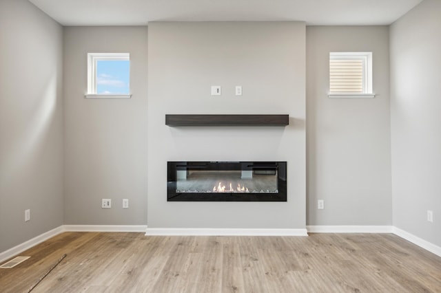 unfurnished living room featuring a glass covered fireplace, visible vents, baseboards, and wood finished floors